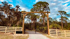 Un arco in legno con un cancello in metallo, circondato da una staccionata e alberi.