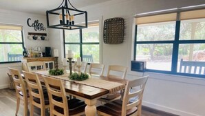 Zona pranzo con tavolo e sedie in legno, un lampadario e un cartello con scritto 'Coffee Bar'.
