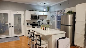A modern kitchen with white cabinets, a stainless steel refrigerator, a microwave, and a large island with bar stools. - You'll be so happy, you'll want to "Just Dance" (Dandridge)