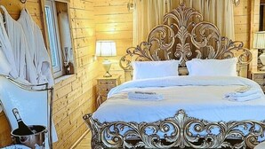 A wooden cabin bedroom with a large bed, a nightstand with a lamp, and a decorative headboard.
