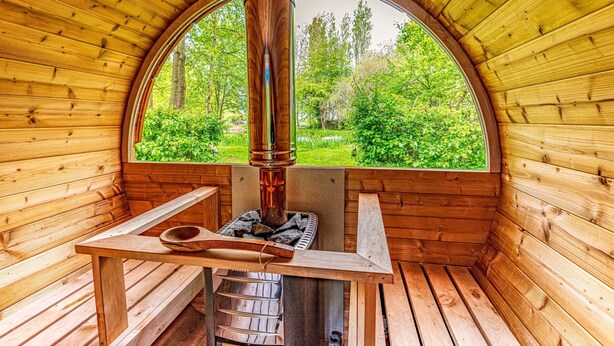 A wooden sauna with a large arched window, a wooden bench, and a central heating pipe.