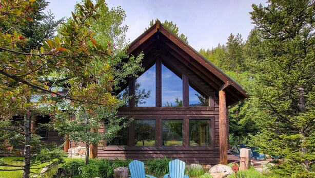 A cabin with a large window, wooden exterior, and a garden with rocks and plants.