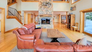 A spacious living area with a stone fireplace, leather sofas, a wooden coffee table, and a staircase leading to an upper level.