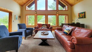 A spacious living room with a high ceiling, large windows, and a fireplace.