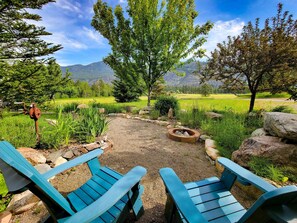 A patio with two blue Adirondack chairs, a fire pit, and a view of a mountainous landscape. - Fireside Lodge - spacious home in Mazama (Winthrop)