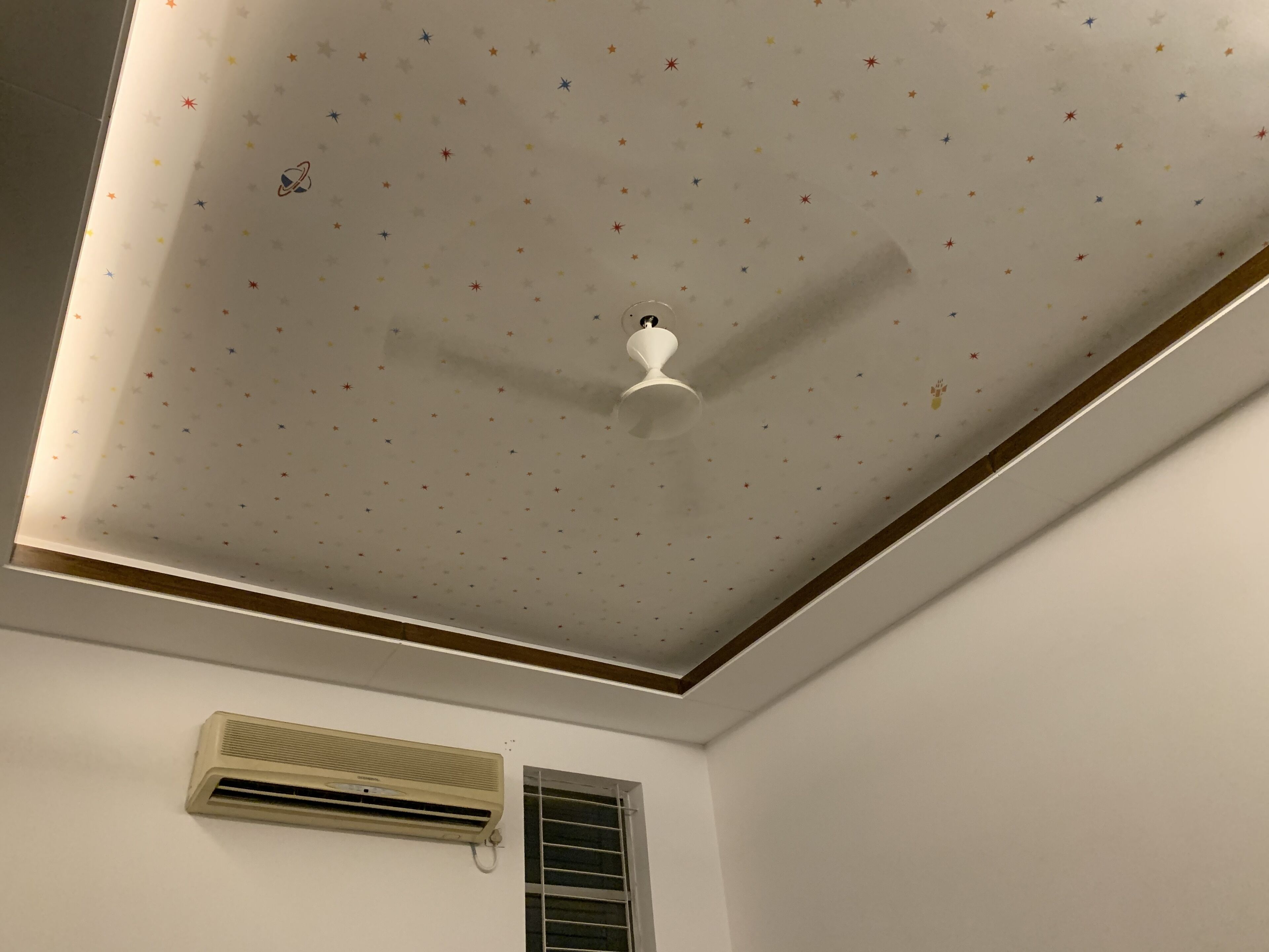 A room with a white ceiling featuring a star pattern, a white ceiling fan, and a wall-mounted air conditioner.