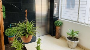 Un intérieur moderne avec un ascenseur noir, des plantes en pot et une fenêtre équipée de stores.