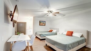 Une chambre avec deux lits, un bureau et un ventilateur de plafond.