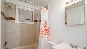 Ein Badezimmer mit Badewanne, Toilette, Waschbecken und einem Fenster mit Jalousien.