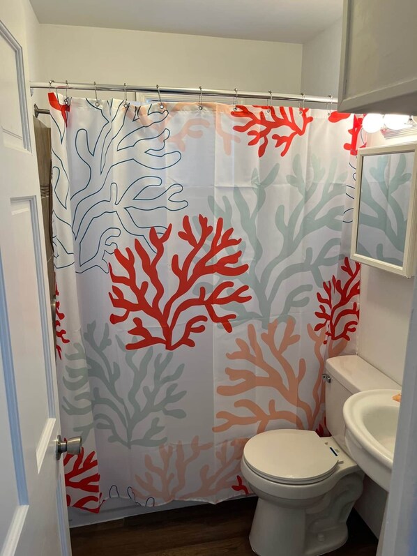 A bathroom with a shower curtain featuring coral patterns, a toilet, and a sink. - One Bedroom Suite 107 (Wildwood)