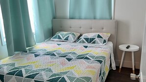 A bedroom with a bed, a bedside table, a ceiling fan, and curtains. - One Bedroom Suite 107 (Wildwood)