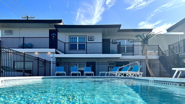 A swimming pool with clear water, surrounded by a fenced area with lounge chairs. - One Bedroom Suite 107 (Wildwood)