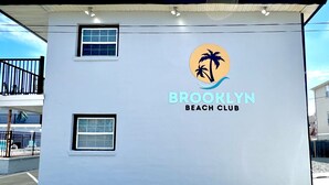A building with the sign "Brooklyn Beach Club" and a logo featuring palm trees. - One Bedroom Suite 107 (Wildwood)