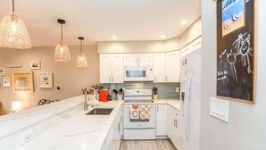 A modern kitchen with white cabinets, a large island, a microwave, and a stove. - Sojourn The Ocean Breeze in Virginia Beach (Virginia Beach)