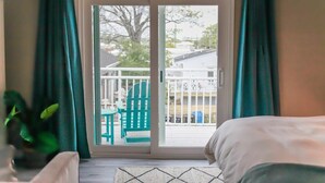 A bedroom with a bed, a view through a sliding glass door to an outdoor area with a chair and a fence. - Sojourn The Ocean Breeze in Virginia Beach (Virginia Beach)