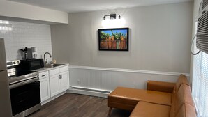 Eine moderne Küche mit weißen Schränken, einer schwarzen Mikrowelle und einem Edelstahlherd. Es gibt eine braune Lederecke und ein gerahmtes Bild an der Wand.