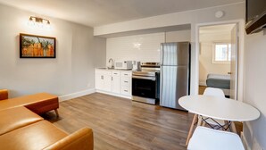 Una cocina moderna con gabinetes blancos, horno integrado y refrigerador. Cuenta con una zona de comedor con una mesa y sillas blancas.