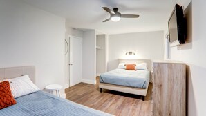 Ein Schlafzimmer mit zwei Betten, einem Deckenventilator, einem an der Wand montierten Fernseher und einem kleinen weißen Tisch.