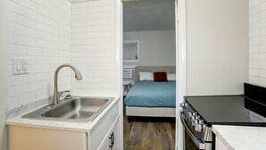 A compact kitchen with a sink, stove, and a small dining area. - Deluxe Queen One Bedroom Suite 206 (Wildwood)