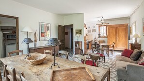 Un comedor con mesa de madera, sillas y una lámpara. Cuenta con una zona de cocina con armarios y un microondas.