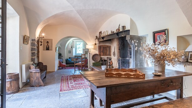 Un interior rústico con una mesa de madera, paredes de piedra y una chimenea.