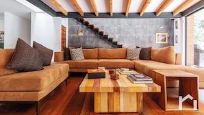 Een moderne woonkamer met een houten salontafel, een hoekbank en een trap tegen een betonnen muur.