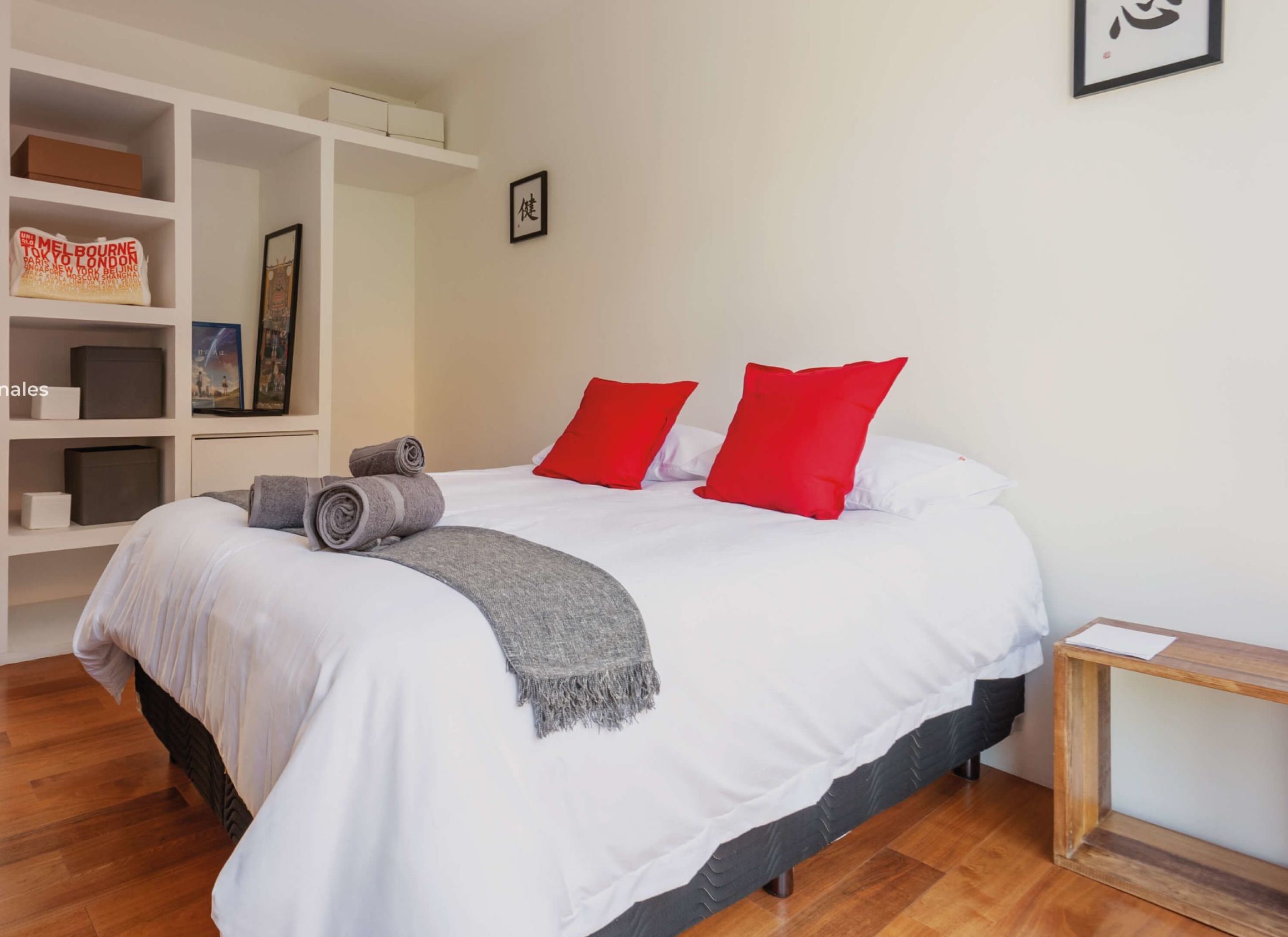 A bedroom with a queen-sized bed, a private bathroom, storage shelves, and a wooden desk.