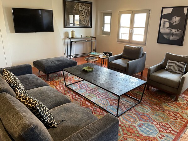 A living room with a sofa, armchairs, a coffee table, a TV, and artwork on the walls. - The Bell Tower Apartment (Aix-en-Provence)