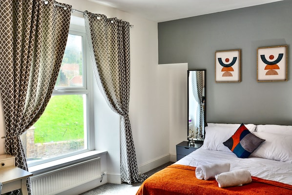 A hotel room with a bed, a nightstand, a mirror, and a window with curtains.