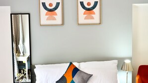 A neatly made bed with white linens and an orange throw blanket, a modern abstract painting on the wall, and a mirror reflecting part of the room. - Captivating 3-bed House in Swansea Town Center (Swansea)