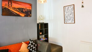 A living room with a sofa, a bookshelf, a cityscape painting, and a 'Let's stay home' sign. - Captivating 3-bed House in Swansea Town Center (Swansea)