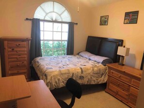 Cozy retreat with a single bed, dresser, and desk, offering a peaceful view of the outdoors.
