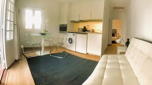 A compact living space with a kitchenette, a washing machine, a dining area with a glass table, and a sofa.