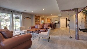 A spacious living room with a leather sofa, a coffee table, and a dining area with a kitchen in the background. - Walkout: Raspberry Mountain Family Farmhouse (Monument)