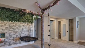 A room with a stone wall, a hanging swing, and a tree-like structure with hanging elements. - Walkout: Raspberry Mountain Family Farmhouse (Monument)