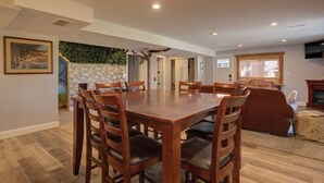 A spacious dining area with a large wooden table and chairs, a stone wall with greenery, and a cozy seating area with a fireplace. - Walkout: Raspberry Mountain Family Farmhouse (Monument)