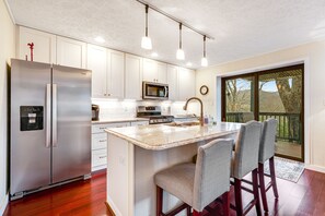 A modern kitchen with white cabinets, stainless steel appliances, and a large island with bar stools. - Mountain view condo with deck, gas fireplace, WiFi, W/D, & central AC (Sugar Mountain)