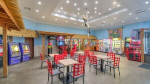 Restaurante com mesas internas, jogos de fliperama e área com telhado de palha.