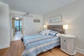 A bedroom with a bed, bedside lamps, a nightstand, a wooden headboard, and a view of the balcony.