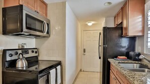 Cocina compacta con estufa, microondas, refrigerador y encimera de granito.