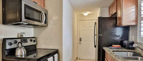 A compact kitchen with a stove, microwave, refrigerator, and granite countertop.