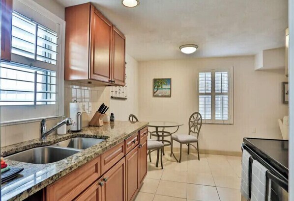 A kitchen with granite countertops, wooden cabinets, a sink, and a dining area with a table and chairs.