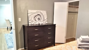 Une chambre à coucher comprenant un lit, une commode, un placard et une œuvre d’art en forme de spirale accrochée au mur.