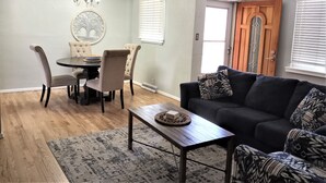 Un coin repas avec une table ronde et des chaises, un canapé agrémenté de coussins à motifs, une table basse en bois et un ventilateur de plafond.