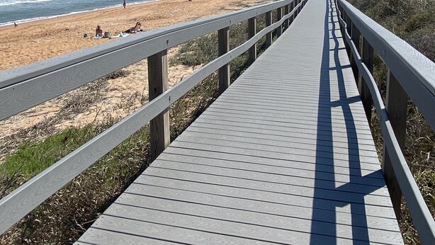 Een houten looppad dat naar een strand leidt, met een pier in de verte.