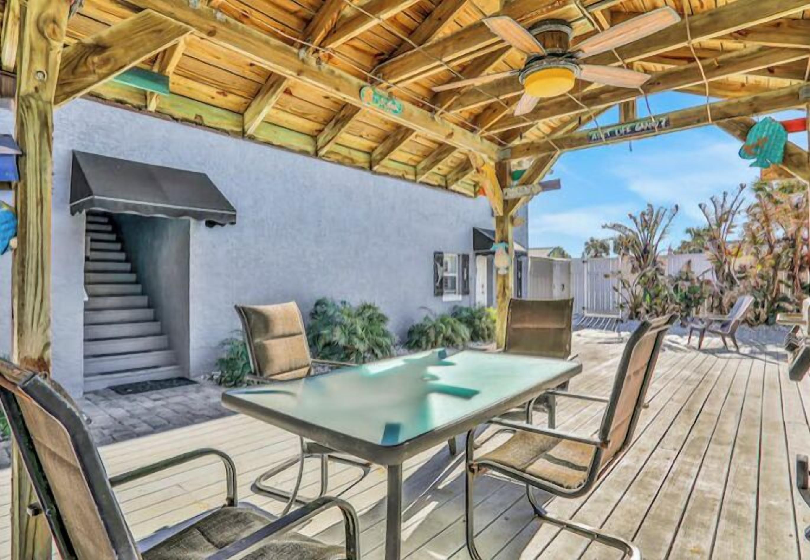 An outdoor patio with a wooden deck, a glass table, and metal chairs.