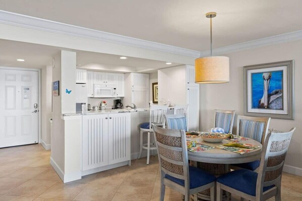 A kitchen with white cabinetry, a dining area with blue chairs, and a pendant light. - Harbour Tower 414 | Gorgeous Residence with Panoramic Water Views and Secluded Beach (Fort Myers)