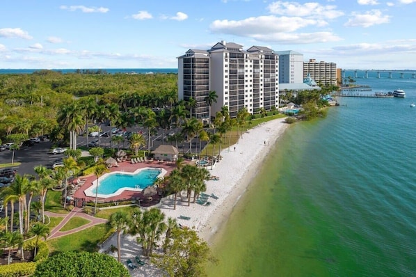 A beachfront hotel with a swimming pool, palm trees, and a view of the ocean.