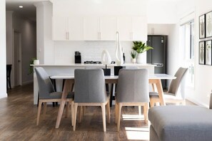 A modern kitchen with white cabinets, a central island, and a dining area with grey chairs and a wooden table.