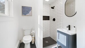 Et badeværelse med et hvidt toilet, en bruseniche med hvide fliser og en vask med et blå skab.